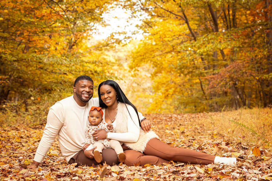 A couple sitting together in the leaves, holding their baby