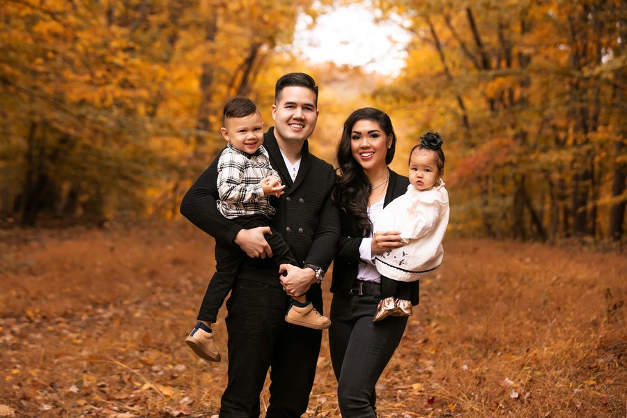 A family of four dressed in black, standing on a golden woodland path