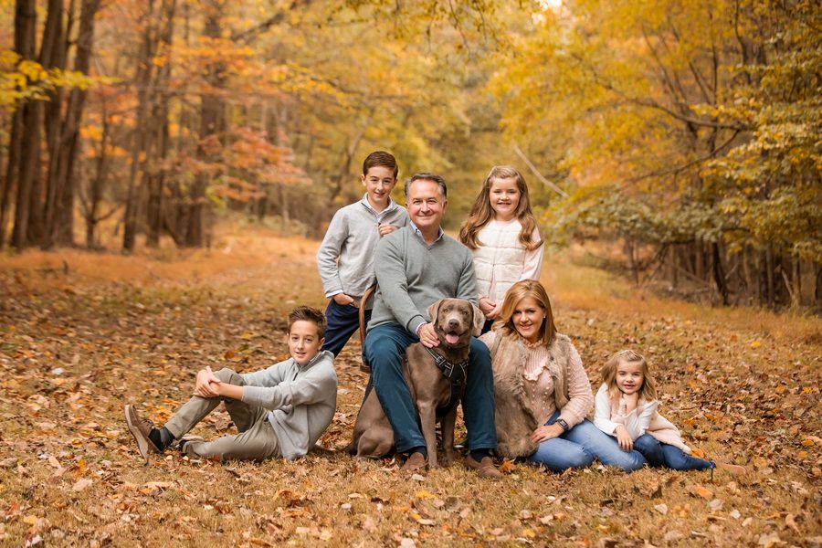 A family of six sitting in the leaves with their dog