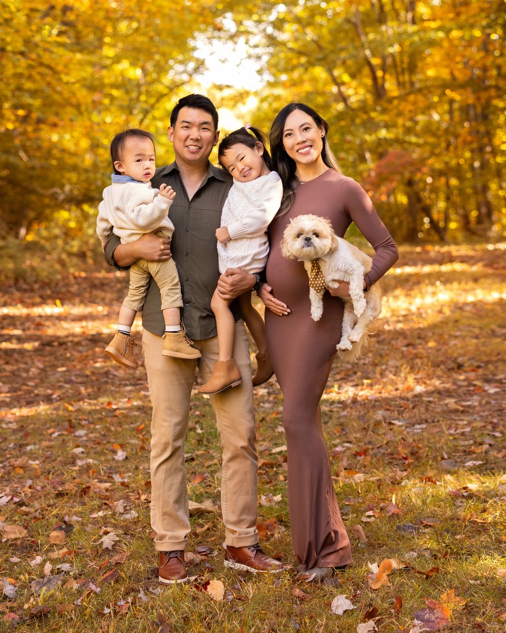 A family with their baby and dog standing among autumn trees