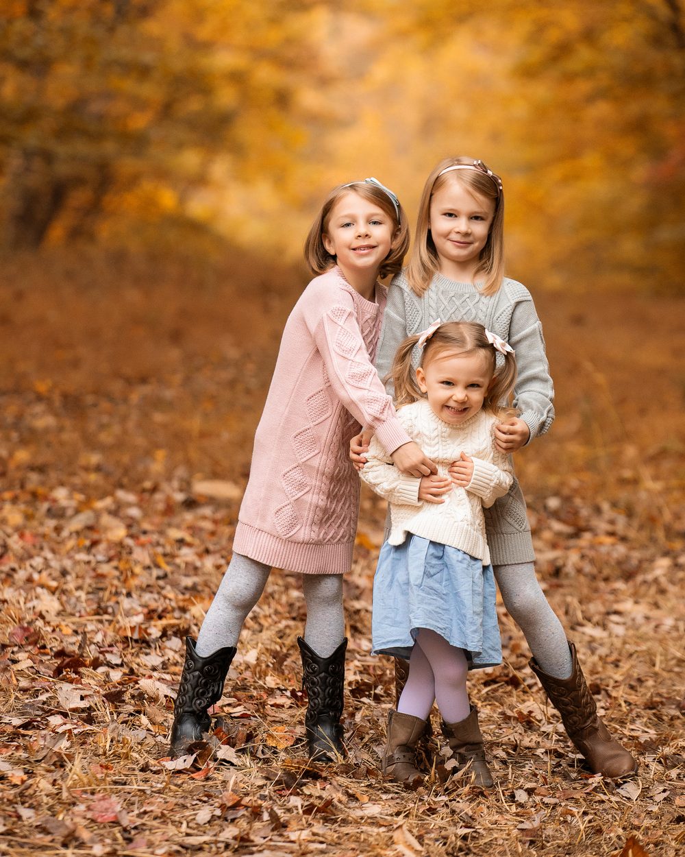 Three girls laughing together among fallen autumn leaves